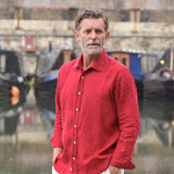 Man wearing a red hemp shirt standing in front of water with boats in the background
