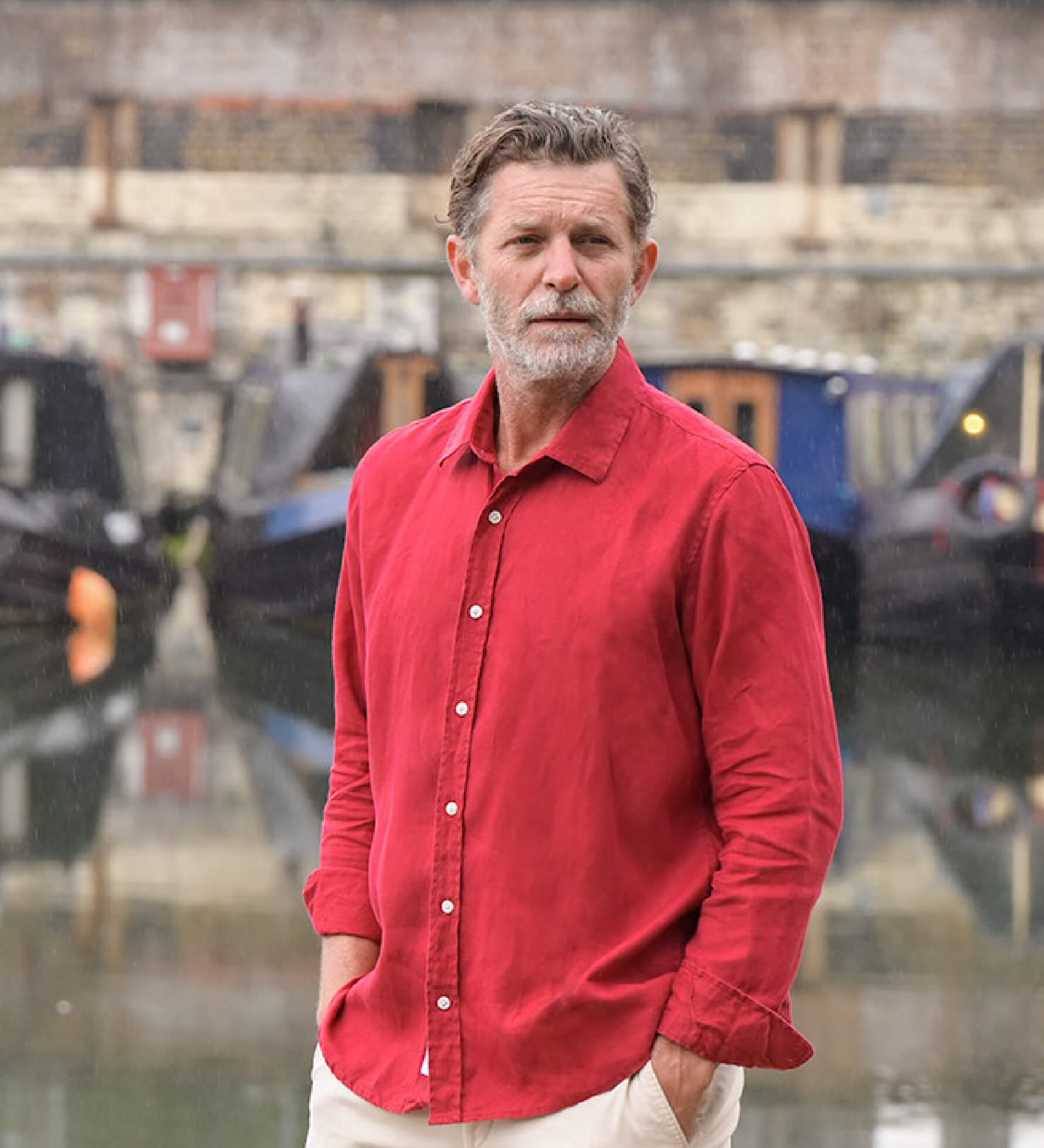Man wearing a red hemp shirt standing in front of water with boats in the background