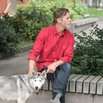 Man in a red shirt sitting on a bench with a dog in an urban setting