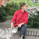 Man in a red shirt sitting on a bench with a dog in an urban setting