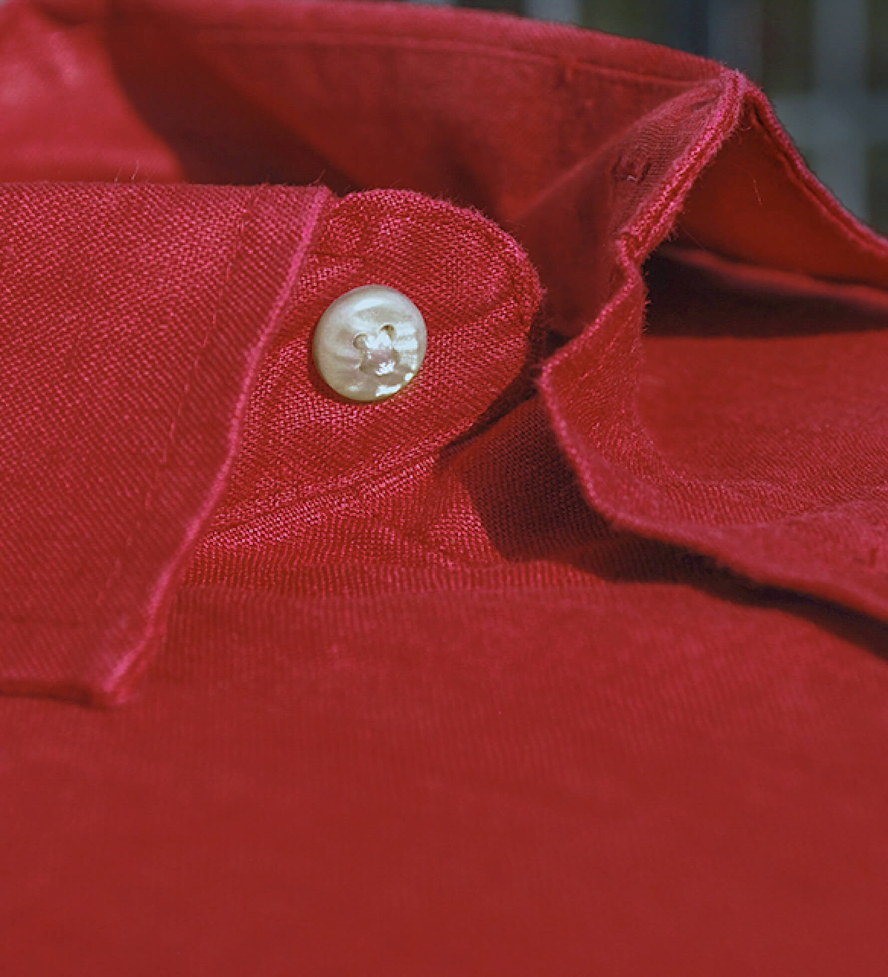 Close-up of a red hemp fabric showing the softness of the fibres with a button on a blurred background