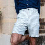 Person wearing light blue striped shorts made from eco-friendly hemp fabric and a dark blue shirt against a stone wall.
