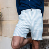 Person wearing light blue striped shorts made from eco-friendly hemp fabric and a dark blue shirt against a stone wall.