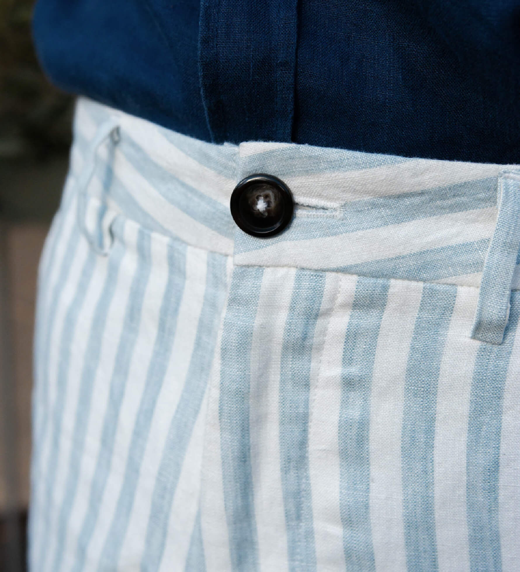 Close-up of blue and white striped hemp shorts with a button, worn with a navy shirt.