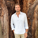 Man in a striped hemp shirt standing against a large tree trunk