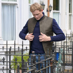 Man wearing a brown nehru jacket over a blue sweater standing in front of a building with decorative railings.