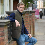 Man wearing a brown hemp nehru jacket leaning against a brick wall on a city street