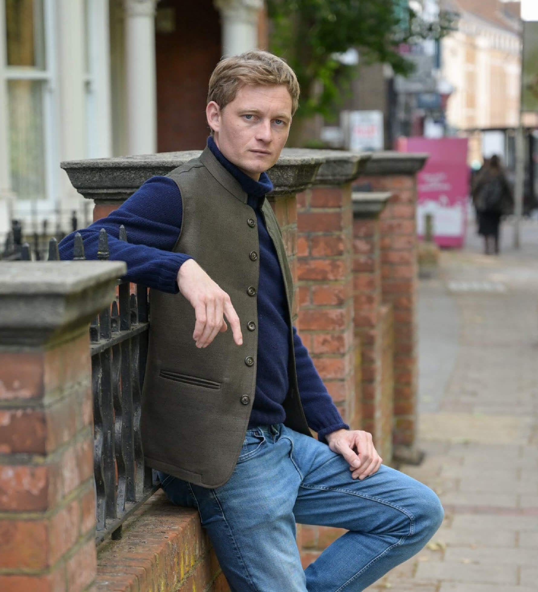 Man wearing a brown hemp nehru jacket leaning against a brick wall on a city street