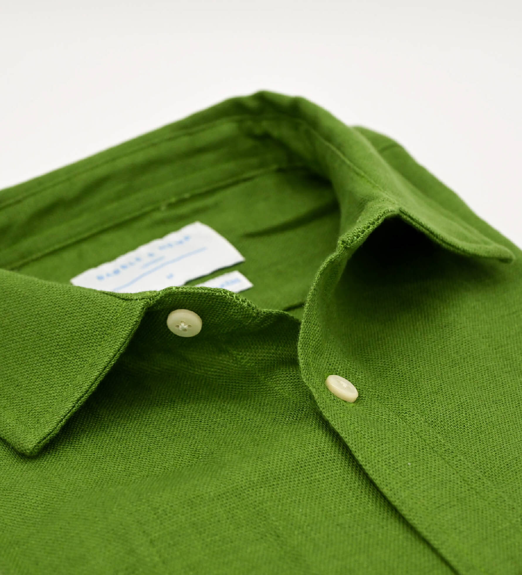 Close-up of a green shirt showing the detail and softness of the hemp fabric with collar and buttons on a white background