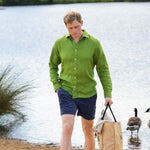 Man in a green shirt and blue shorts standing by a lake with geese in the background