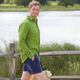 Man in a green shirt and blue shorts standing by a wooden fence with a lake and trees in the background.
