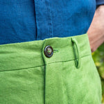 Close-up of green hemp shorts with a button, worn with a blue shirt against a blurred natural background.