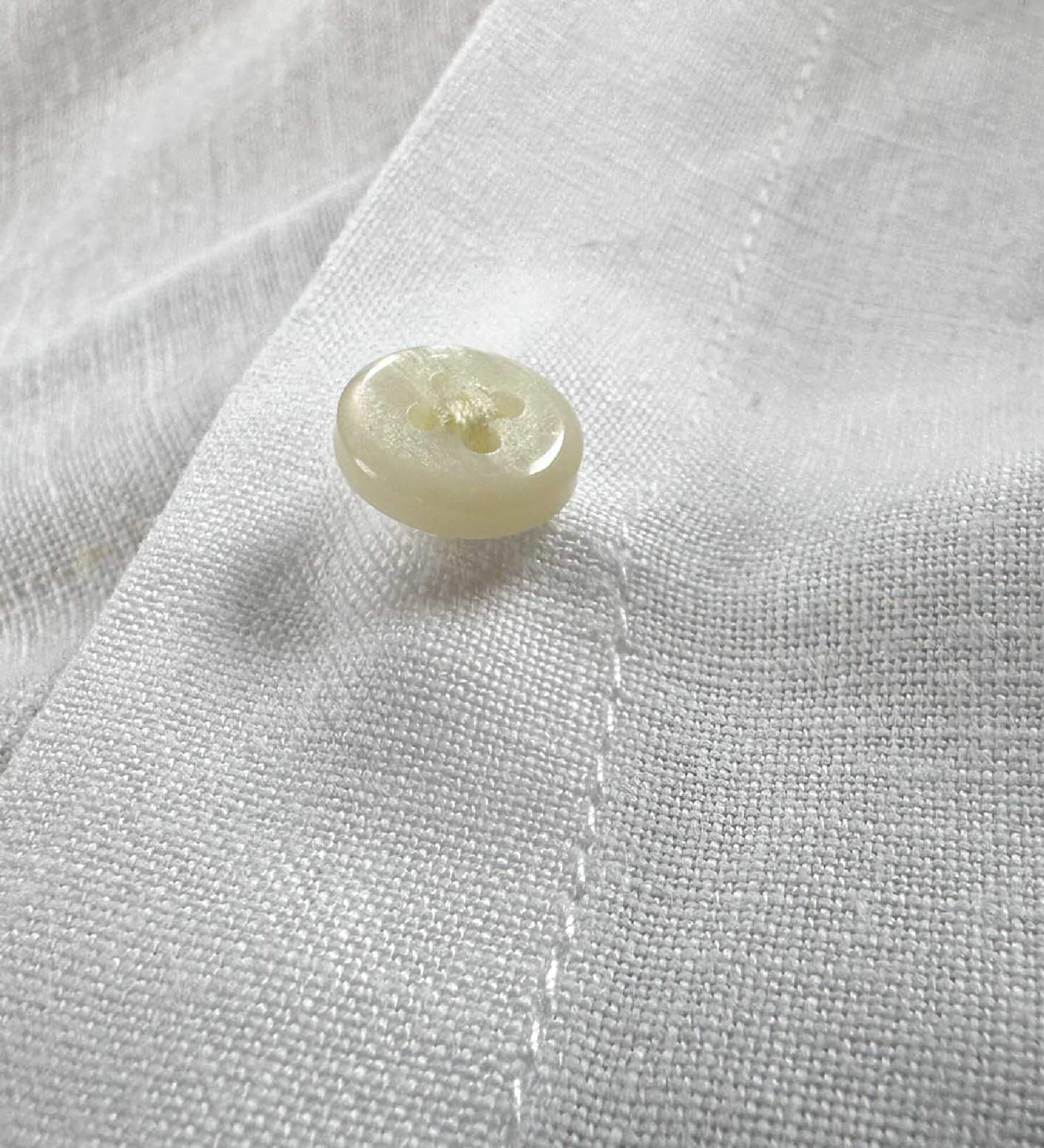 Close-up of a button on white hemp fabric demonstrating the softness of the sustainable hemp fabric
