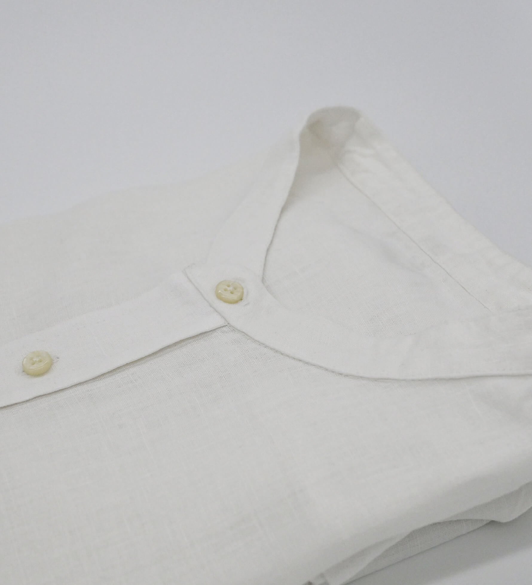 Close-up of a white hemp shirt with mandarin style collar and buttons on a white background