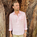 Man wearing a light pink hemp shirt and beige trousers standing in front of a textured tree.