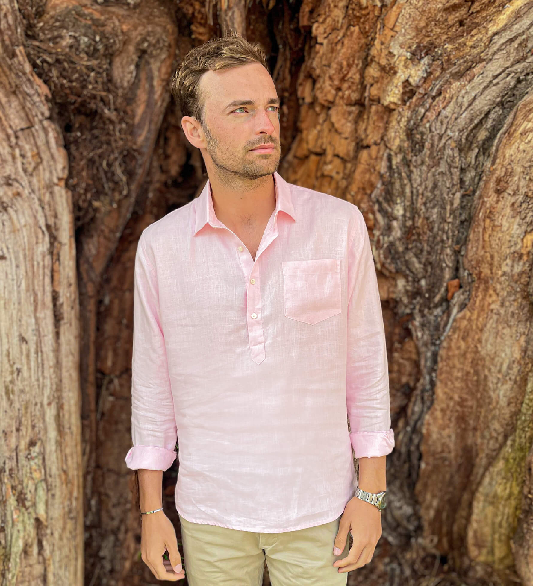 Man wearing a light pink hemp shirt and beige trousers standing in front of a textured tree.