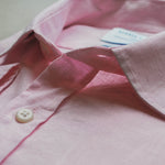 Close-up of a pink shirt with a button and tag on a light background