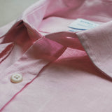 Close-up of a pink shirt with a button and tag on a light background