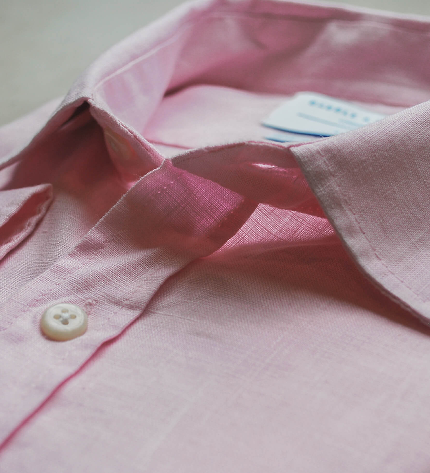 Close-up of a pink shirt with a button and tag on a light background