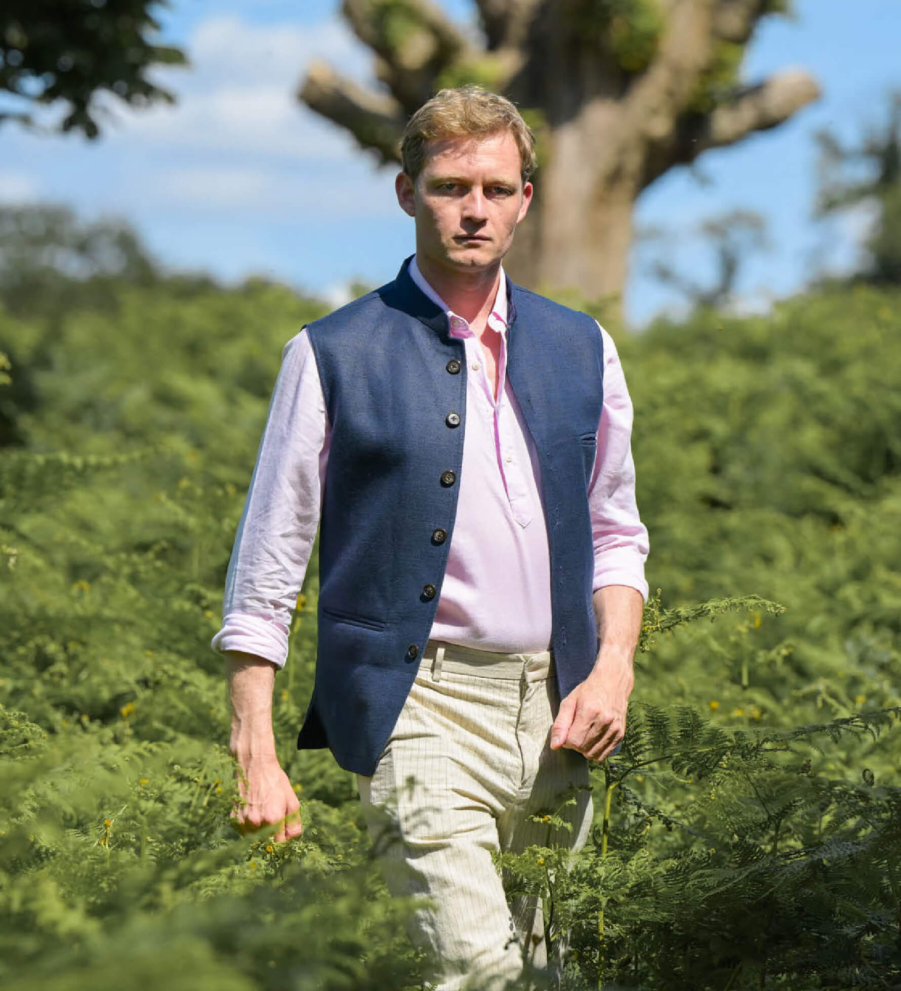Man wearing a blue nehru jacket made from eco-friendly hemp fabric over a pink shirt in a natural setting with trees and greenery.