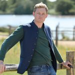 Man standing by a wooden fence with a scenic background of trees and water.