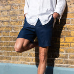 Person wearing navy blue shorts and a white shirt against a brick wall.