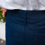 Close-up of a person wearing navy blue shorts from behind showing the pockets on the back in detail and a light-coloured shirt.