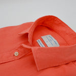 Close-up of an coral coloured hemp shirt with a brand label on a white background