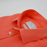 Close-up of an coral coloured hemp shirt with a brand label on a white background