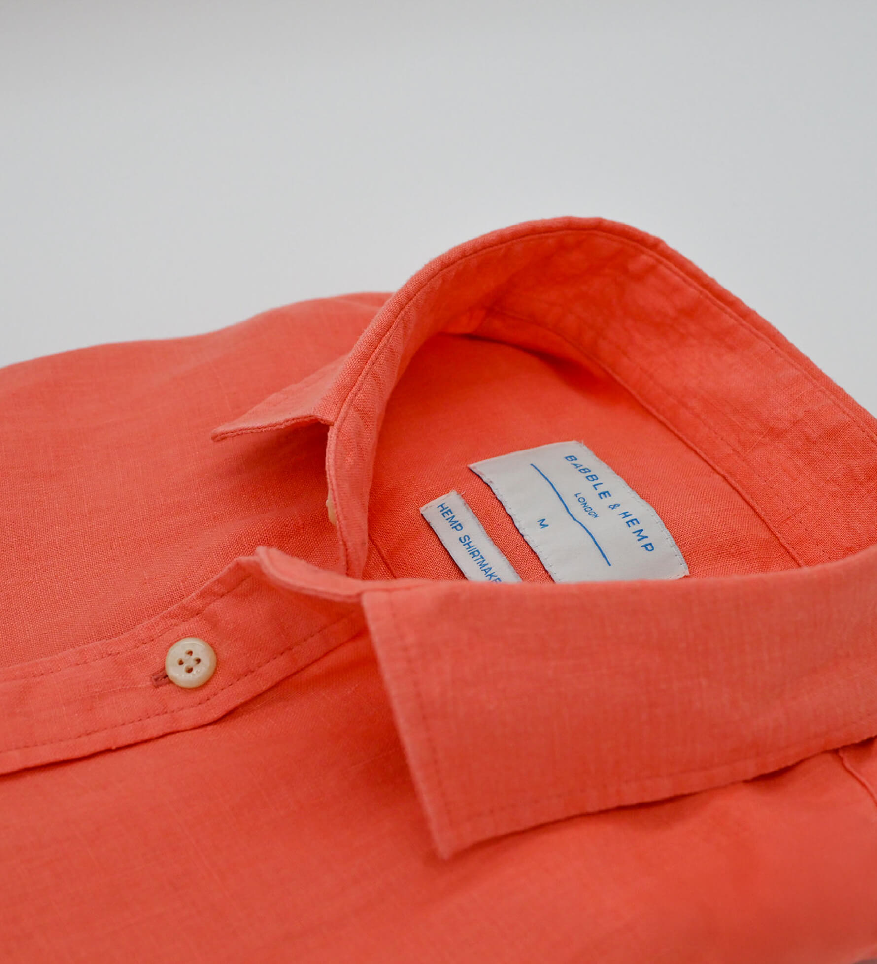 Close-up of an coral coloured hemp shirt with a brand label on a white background