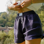 Person wearing dark navy blue hemp boxer shorts with a blurred natural background of hills dropping away behind