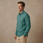 A man wearing a teal green long-sleeve heavy hemp  shirt designed for autumn / winter and khaki pants, standing against a textured beige studio backdrop.