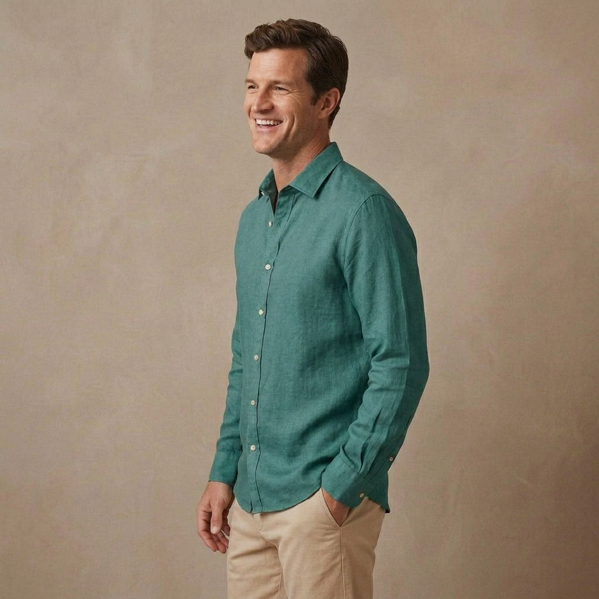 A man wearing a teal green long-sleeve heavy hemp  shirt designed for autumn / winter and khaki pants, standing against a textured beige studio backdrop.