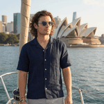 a photo of a man wearing a smart casual, camp collared hemp shirt made from navy blue coloured hemp fabric whilst standing on a yacht