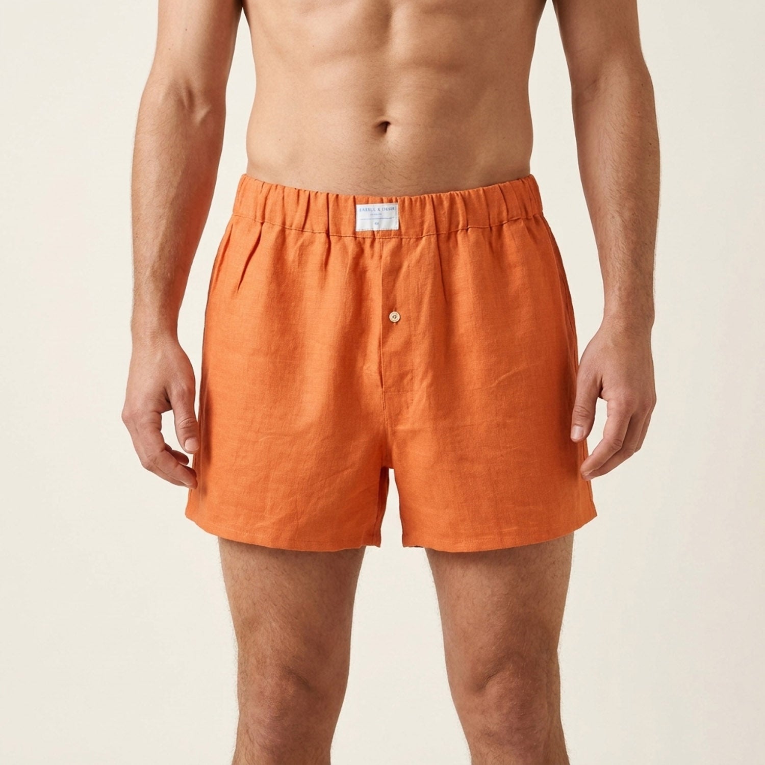 A man wearing bright orange hemp boxer shorts, shown from the chest down against a light beige studio background.