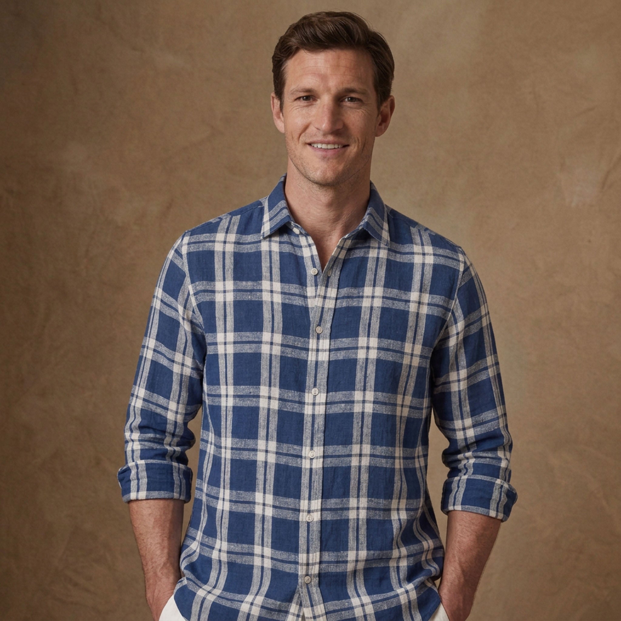 A man wearing a blue and white plaid heavy hemp shirt, standing against a textured brown studio backdrop.
