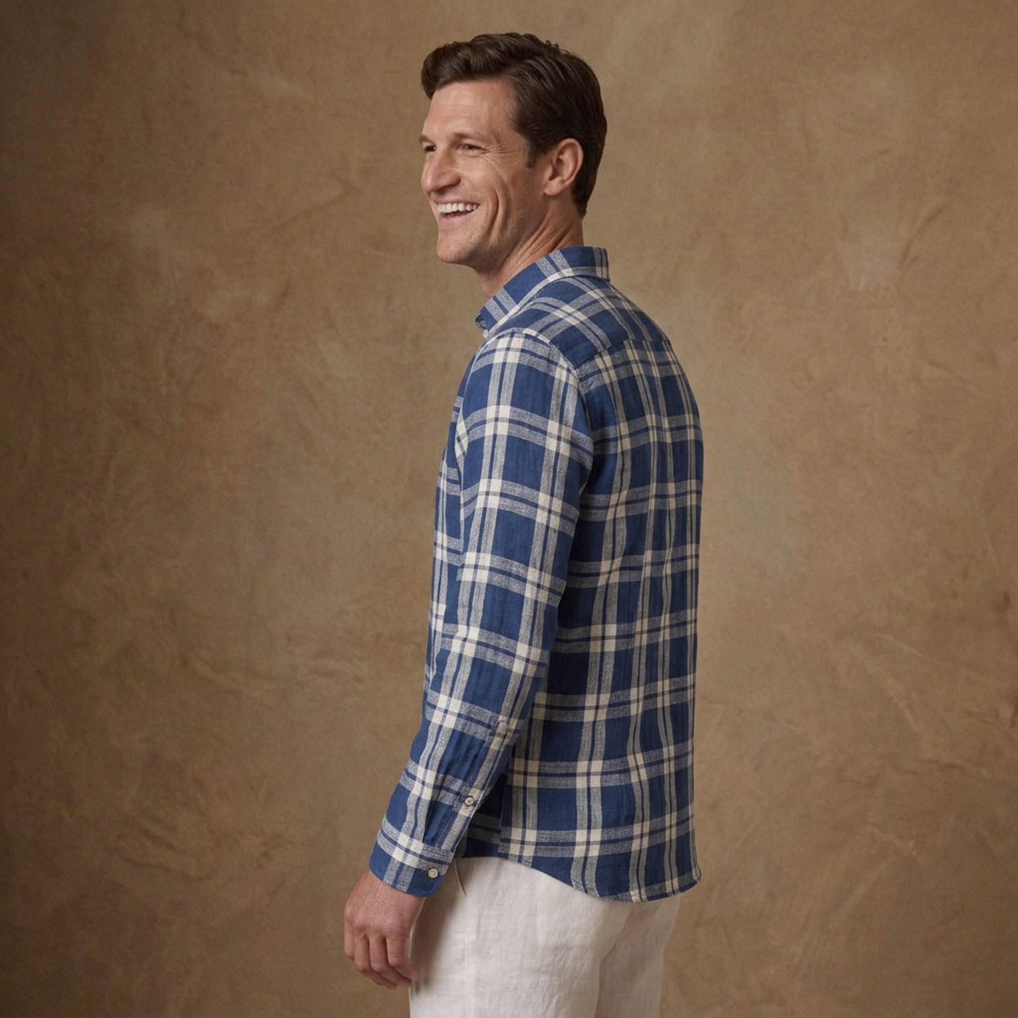 A man wearing a blue and white plaid long-sleeve heavy hemp shirt, shown from a side-back angle against a textured brown studio backdrop.