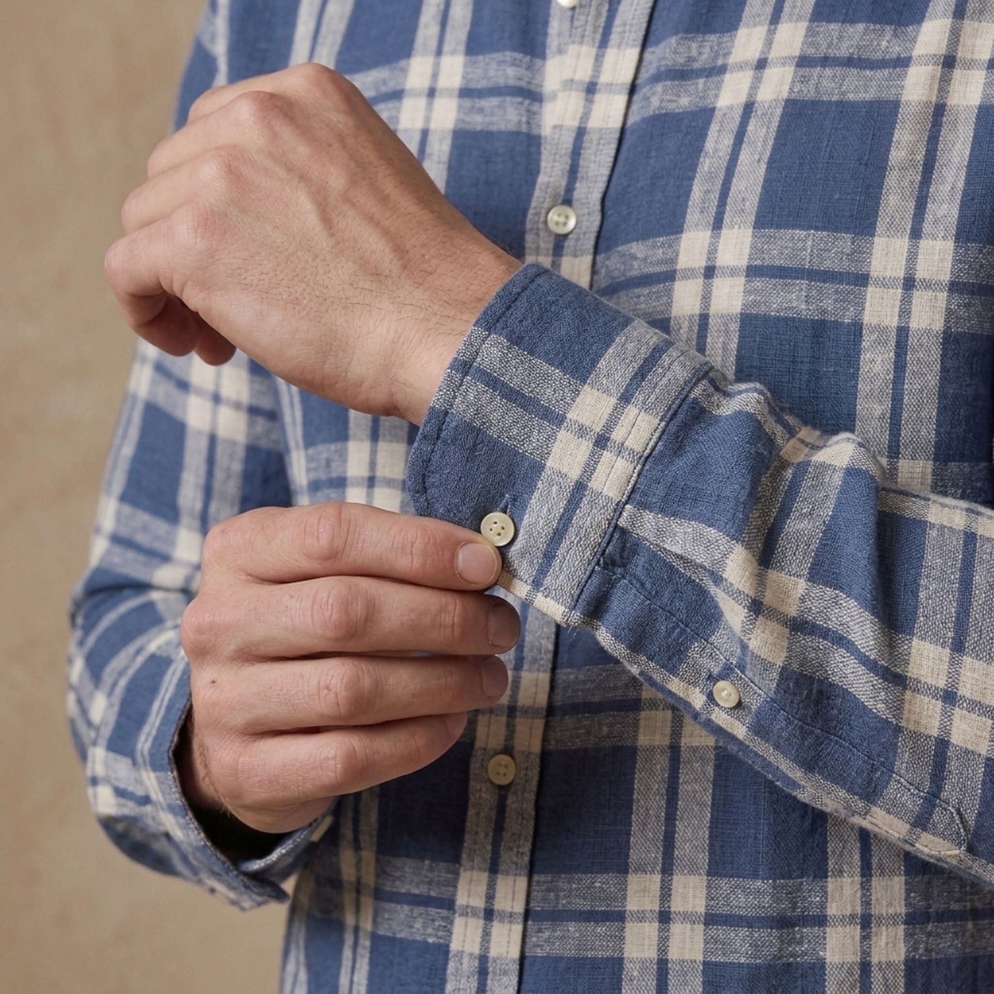 man fastens button on cuff of a blue and white check heavy hemp shirt designed for autumn / winter