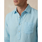 light blue button-up hemp shirt worn by a person on a beige background with focus on the chest pocket and quarter length placket