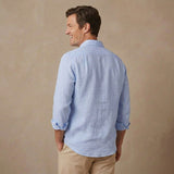 A man wearing a light blue long-sleeve hemp shirt and khaki pants, shown from the back against a textured beige studio backdrop.