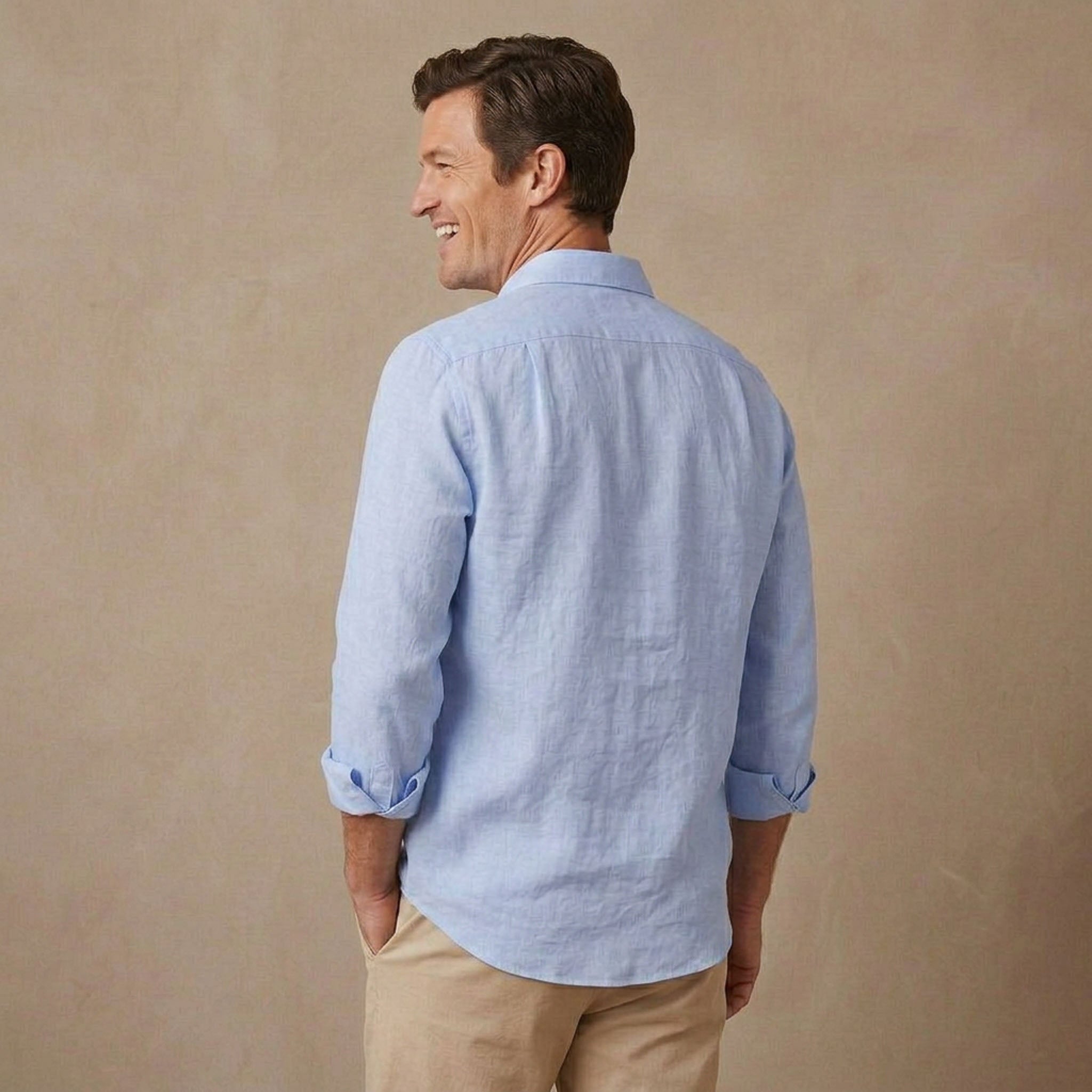 A man wearing a light blue long-sleeve hemp shirt and khaki pants, shown from the back against a textured beige studio backdrop.