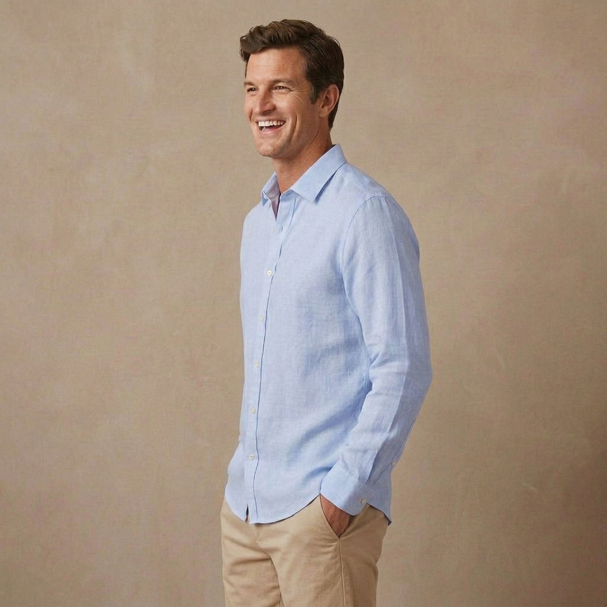 A man wearing a light blue long-sleeve soft hemp shirt and khaki pants, standing against a textured beige studio background.