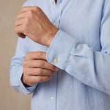 A close-up of a man's hands adjusting the cuff of a light blue hemp shirt.