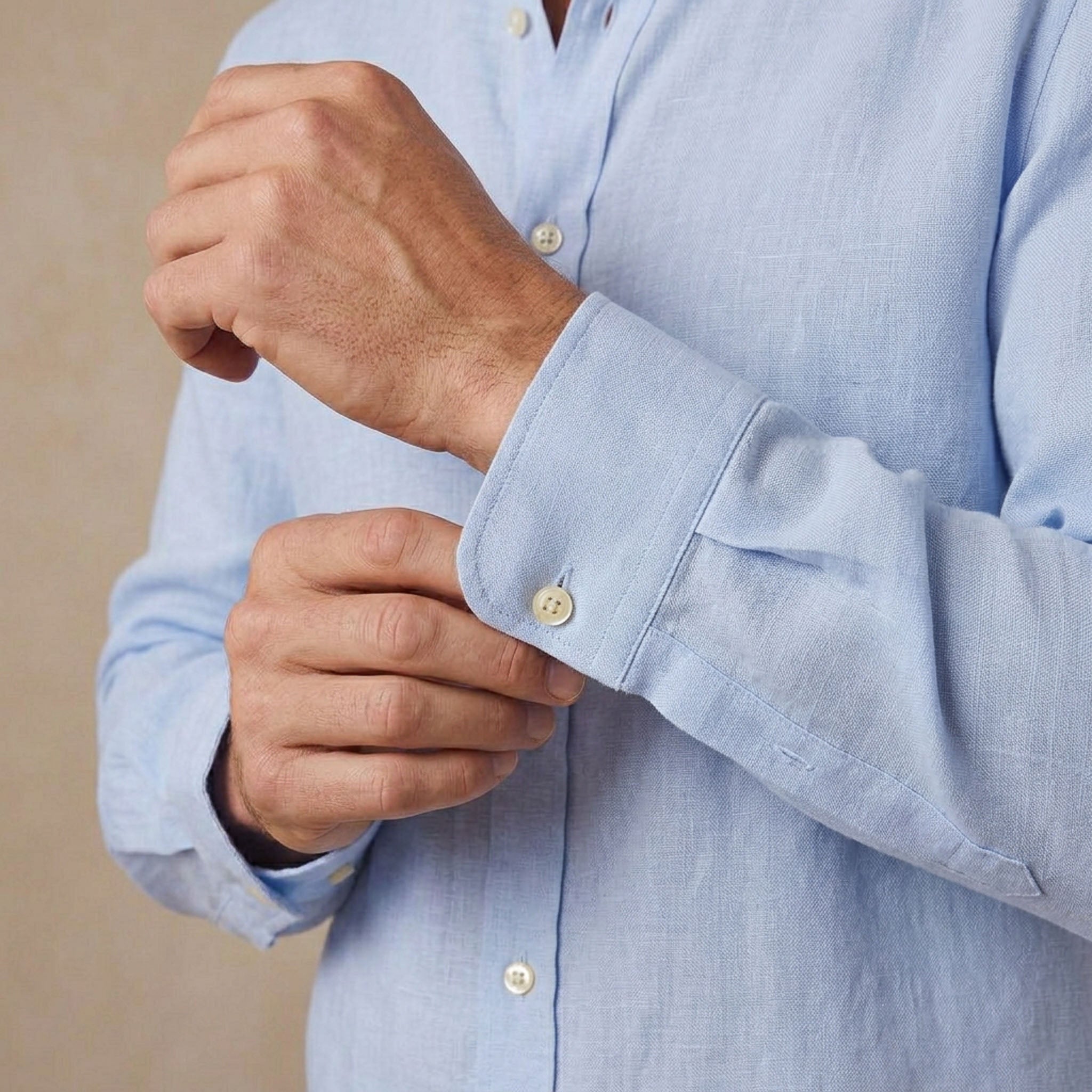 A close-up of a man's hands adjusting the cuff of a light blue hemp shirt.