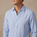 A man wearing a light blue long-sleeve hemp shirt, cropped from the lower face to the chest, against a neutral beige background.