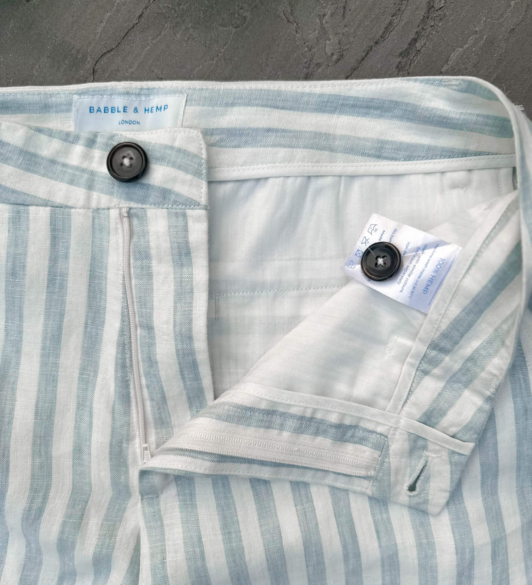 Close-up of a striped blue and white hemp short laid flat with brand labels on a grey surface