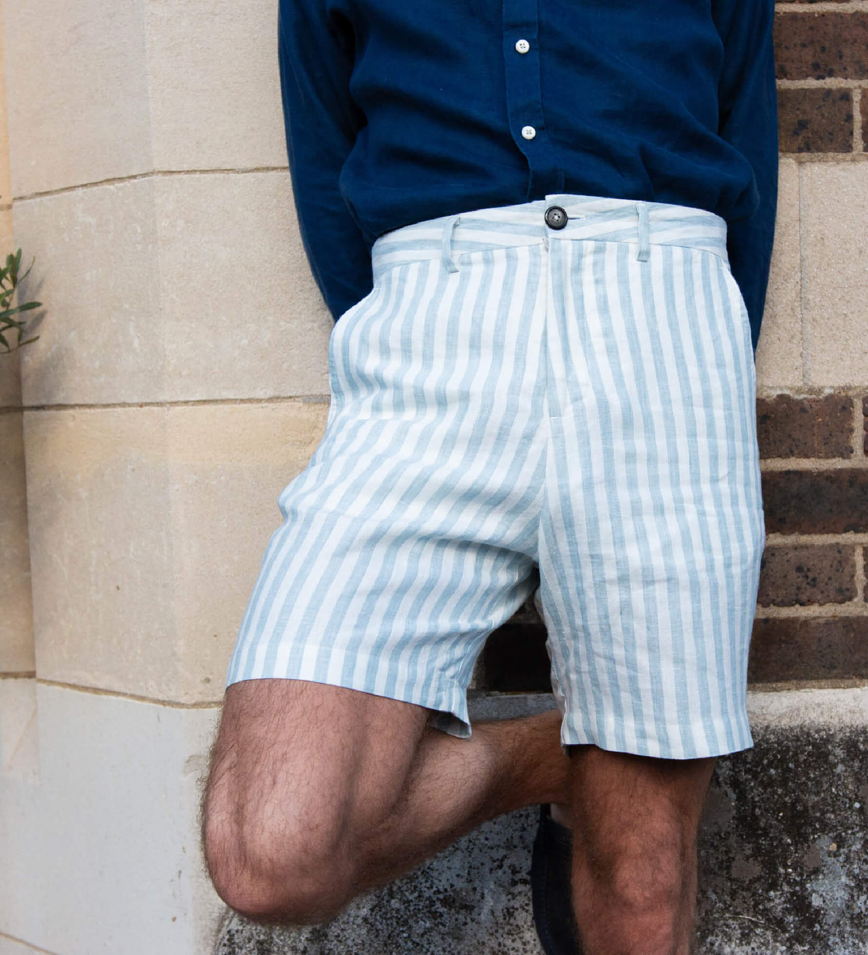 Person wearing light blue striped shorts made from eco-friendly hemp fabric and a dark blue shirt against a stone wall.