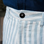 Close-up of blue and white striped hemp shorts with a button, worn with a navy shirt.