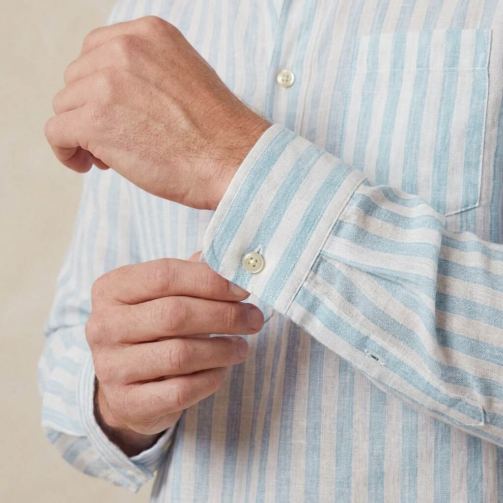 closeup shot of the cuff and button being fastened on a hemp shirt with pocket light blue stripe