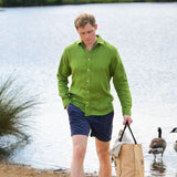 Man in a green shirt and blue shorts standing by a lake with geese in the background